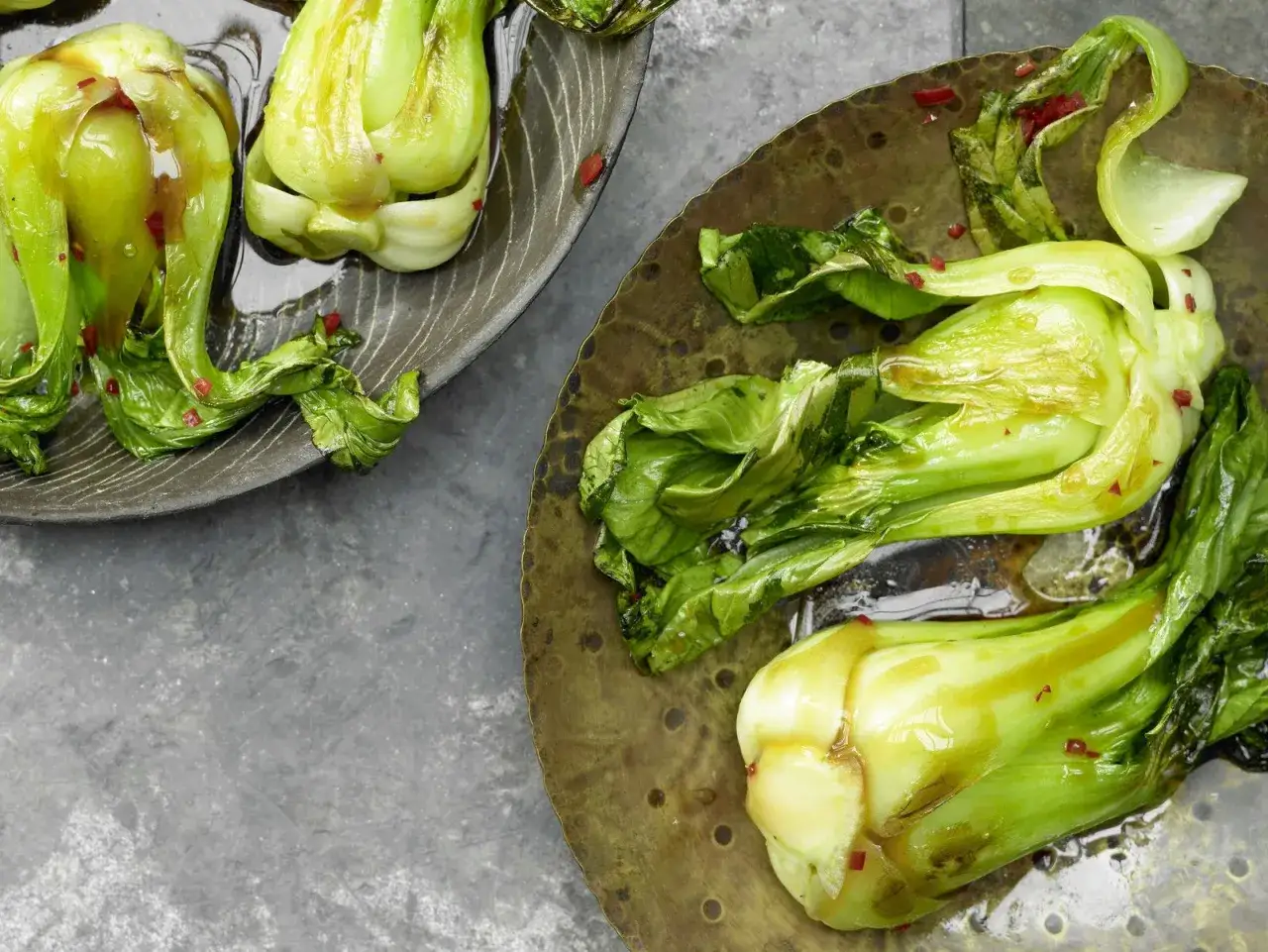 Zubereitetes Pak Choi gl&auml;nzt in einer Sauce auf rustikalen Tellern, bestreut mit roten Chiliflocken.