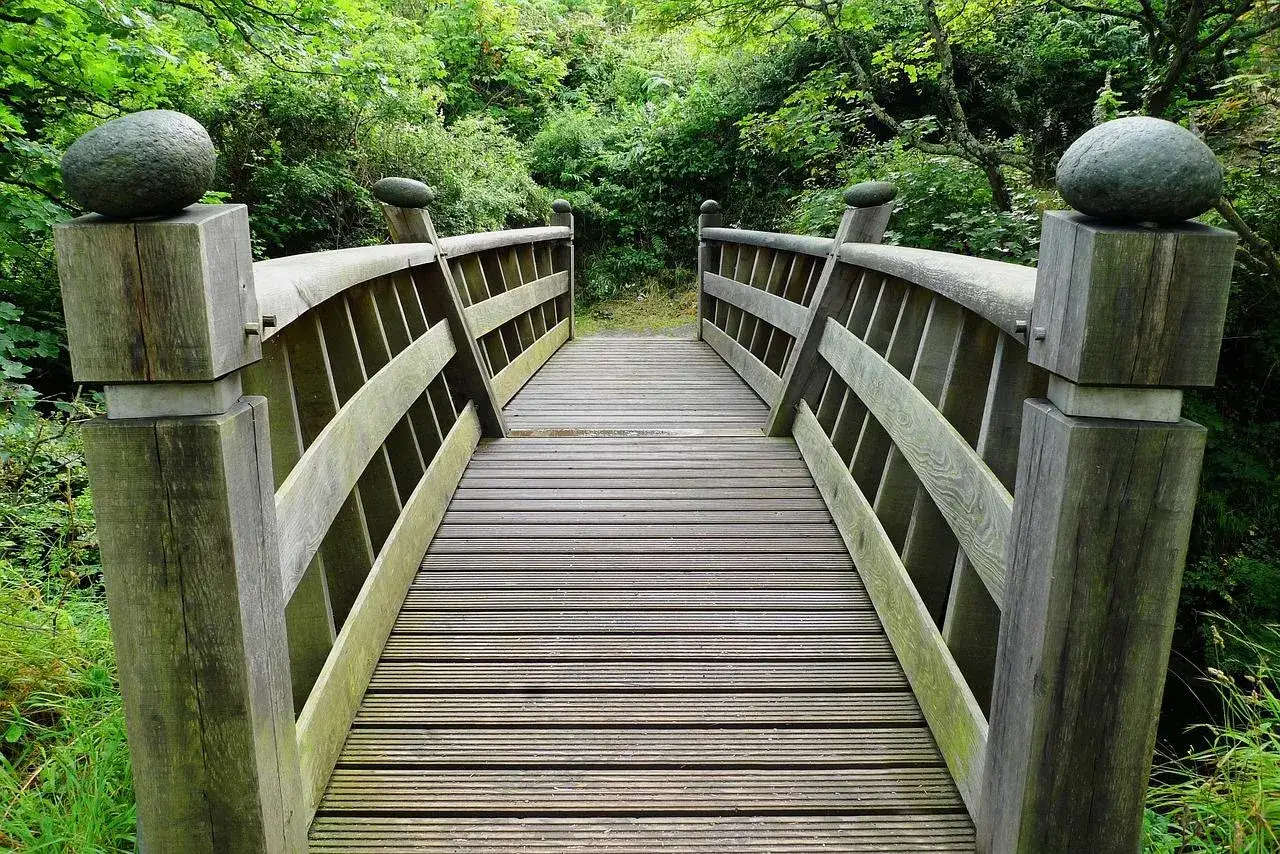 Dos puentes de madera rústicos, adornados con rocas esféricas en sus postes, invitan a cruzar un sendero verde.