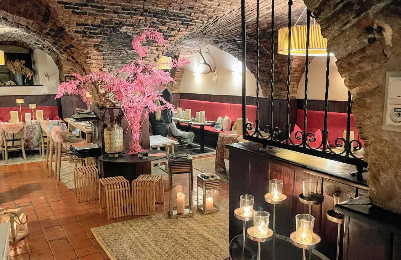 Wnętrze restauracji z ceglanym sklepieniem i czerwonymi ławami. Widać dekoracje, w tym różowe gałązki i świece. To miejsce, gdzie mieści się najstarsza restauracja w Europie.