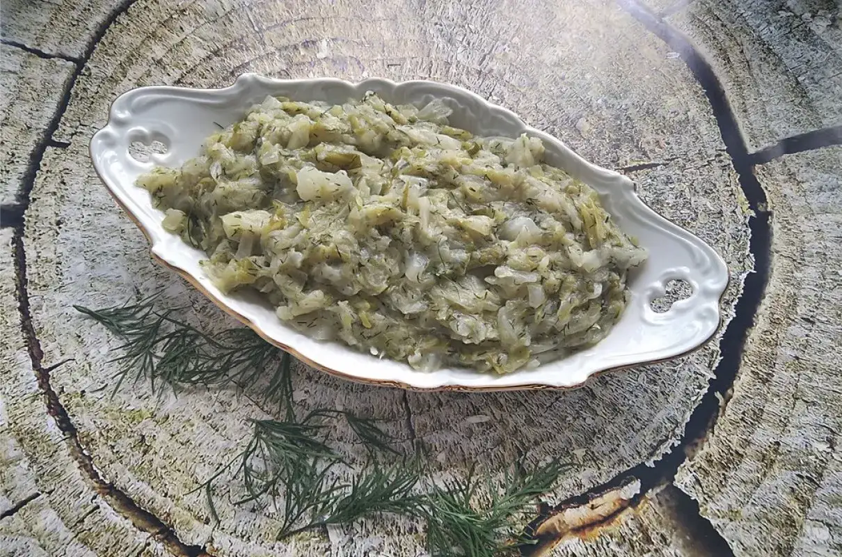 Pyszna kapusta zasmażana z koperkiem, podana w eleganckiej misie na tle drewnianej tekstury.