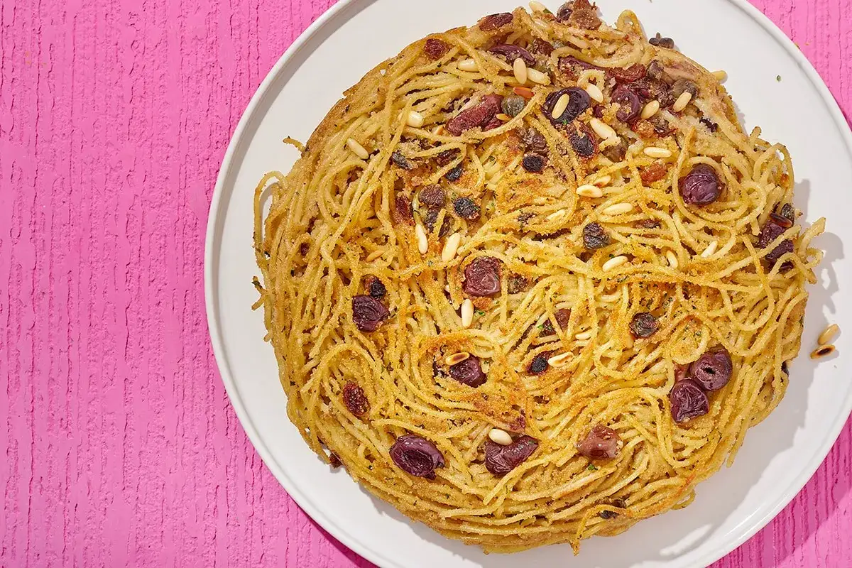 Frittata di scammaro, un tortino di spaghetti dorato con olive, pinoli e uvetta, pronto per essere gustato.
