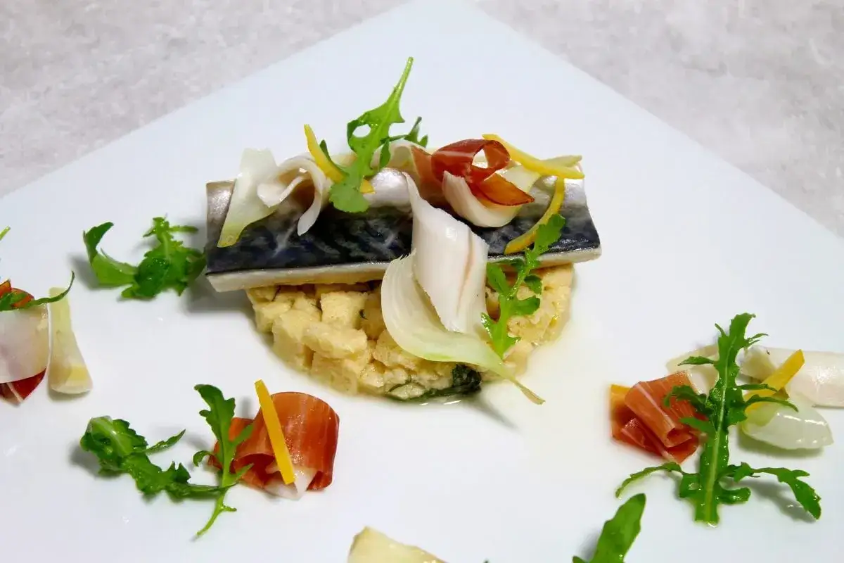 Un délicieux maquereau au vin blanc, servi sur un lit de semoule, garni de fines lamelles de jambon cru, d'oignon et de roquette.