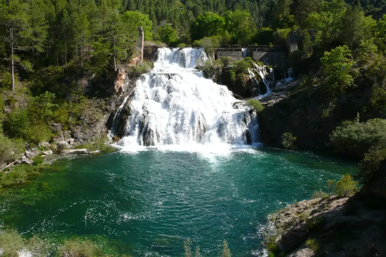 El Salto de Poveda, una cascada imponente con aguas turquesas, rodeada de vegetaci&oacute;n exuberante y ruinas antiguas.