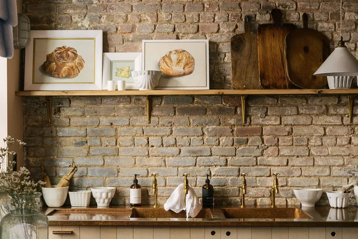 Rusty ceglany backsplash w kuchni, z obrazami chleba i desek do krojenia. Jak zabezpieczyć ścianę w kuchni przed zabrudzeniem? Pomyśl o płytkach lub szkle.