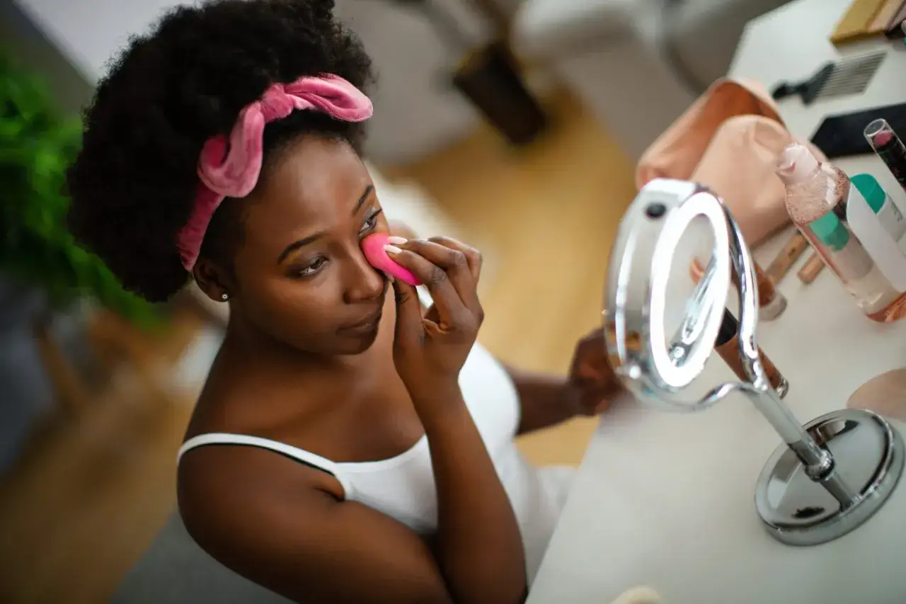 Une femme applique son anti-cerne avant ou après fond de teint, devant un miroir lumineux.