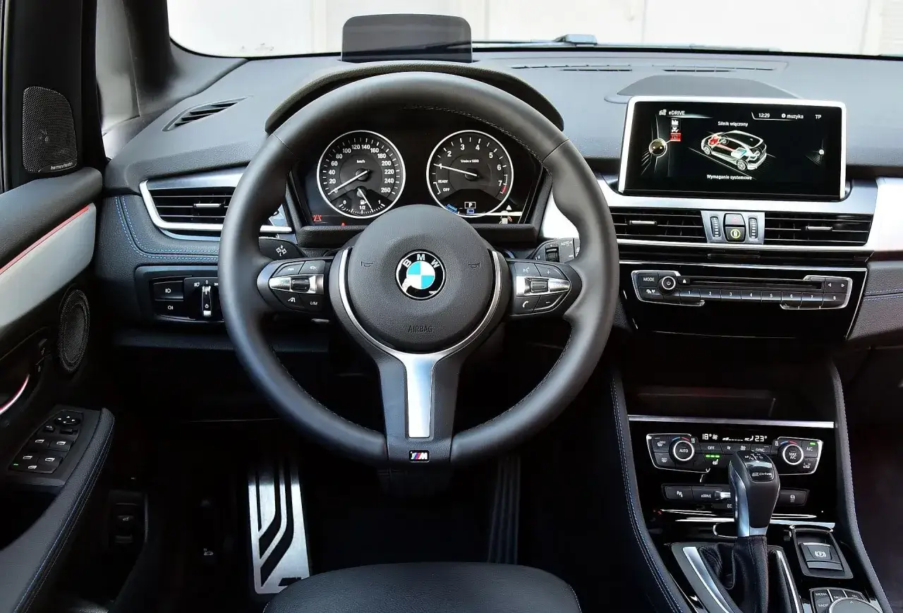 Wnętrze BMW 218i: kierownica M, cyfrowe zegary, ekran multimedialny z grafiką eDRIVE i panel klimatyzacji.