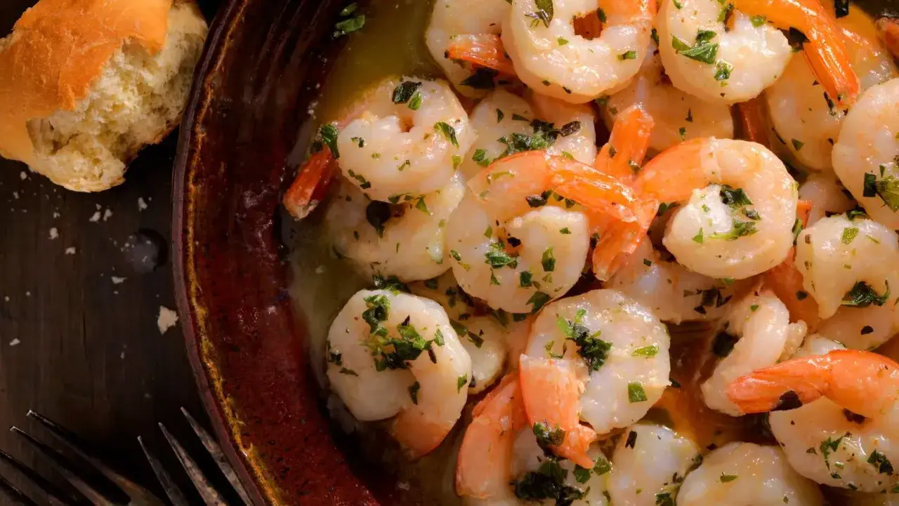 Gambas al ajillo humeantes, con perejil fresco picado, servidas en un cuenco de barro junto a un trozo de pan.
