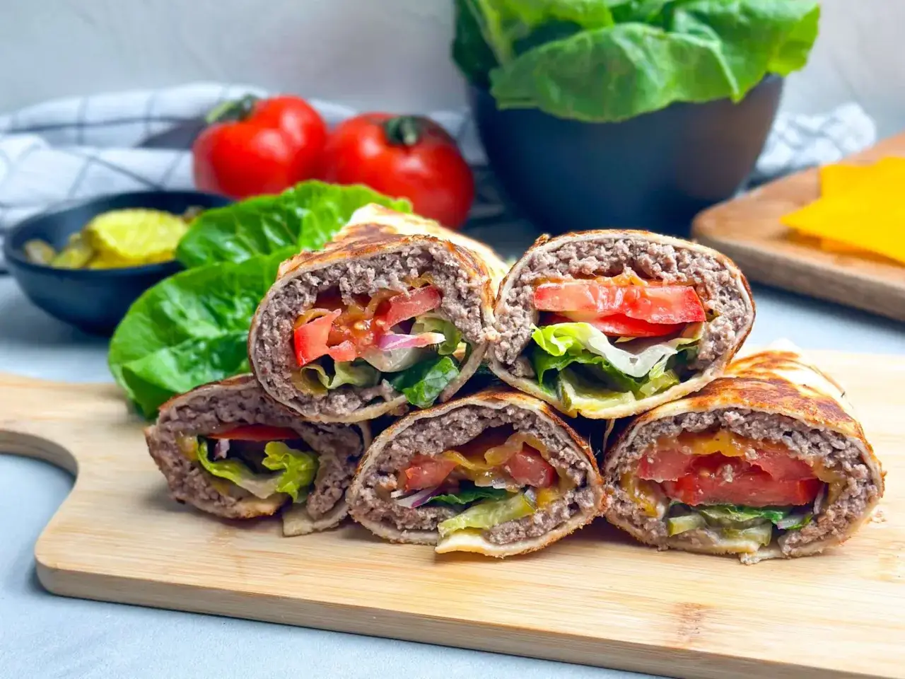 Gestapelte Burger Wraps mit saftigem Rindfleisch, frischem Salat, Tomaten und Gurken auf einem Holzbrett.
