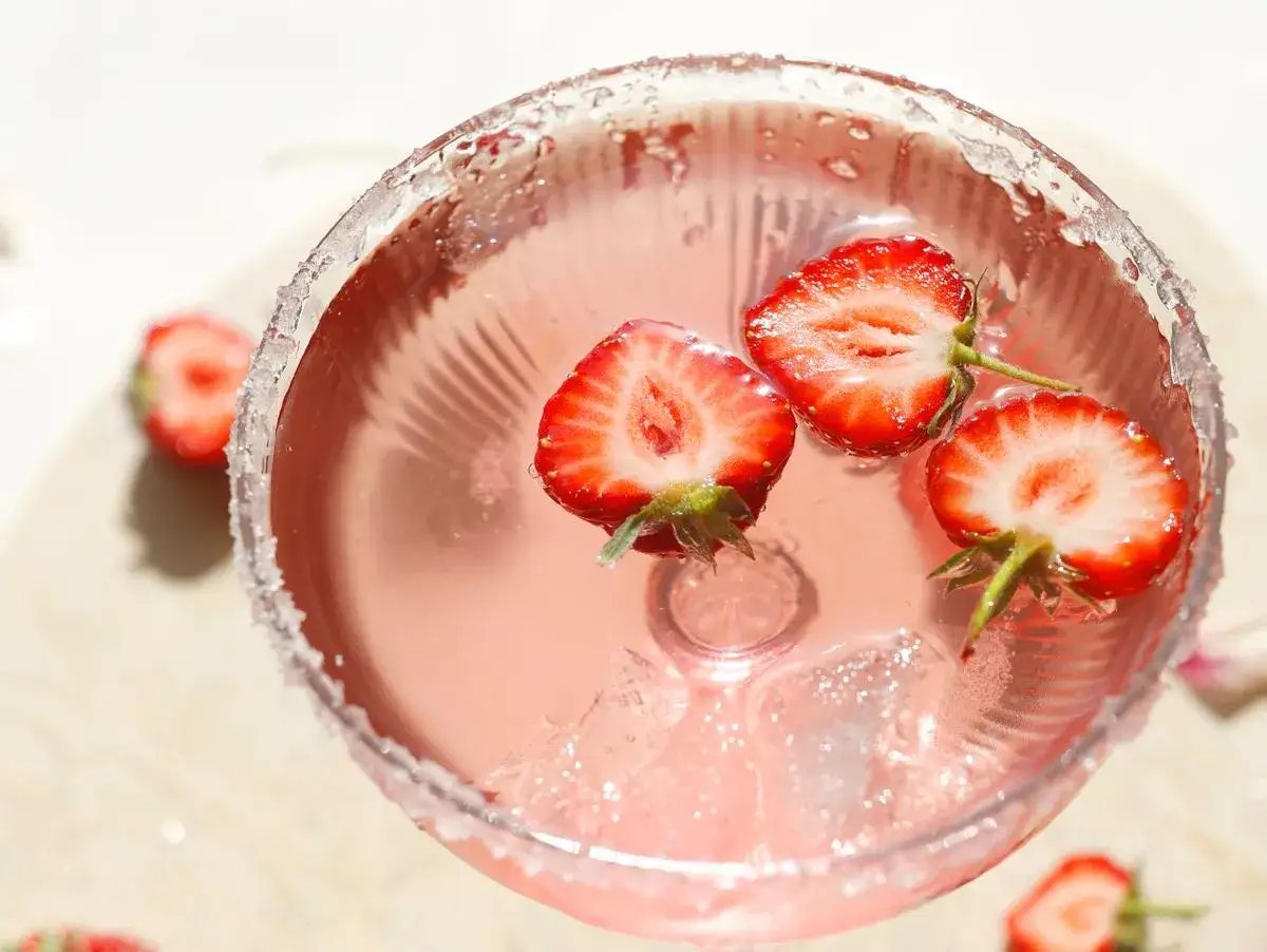 Ein Glas Champagner mit Erdbeeren, das ist pure Erfrischung. Die süßen Früchte schwimmen im rosafarbenen Getränk.