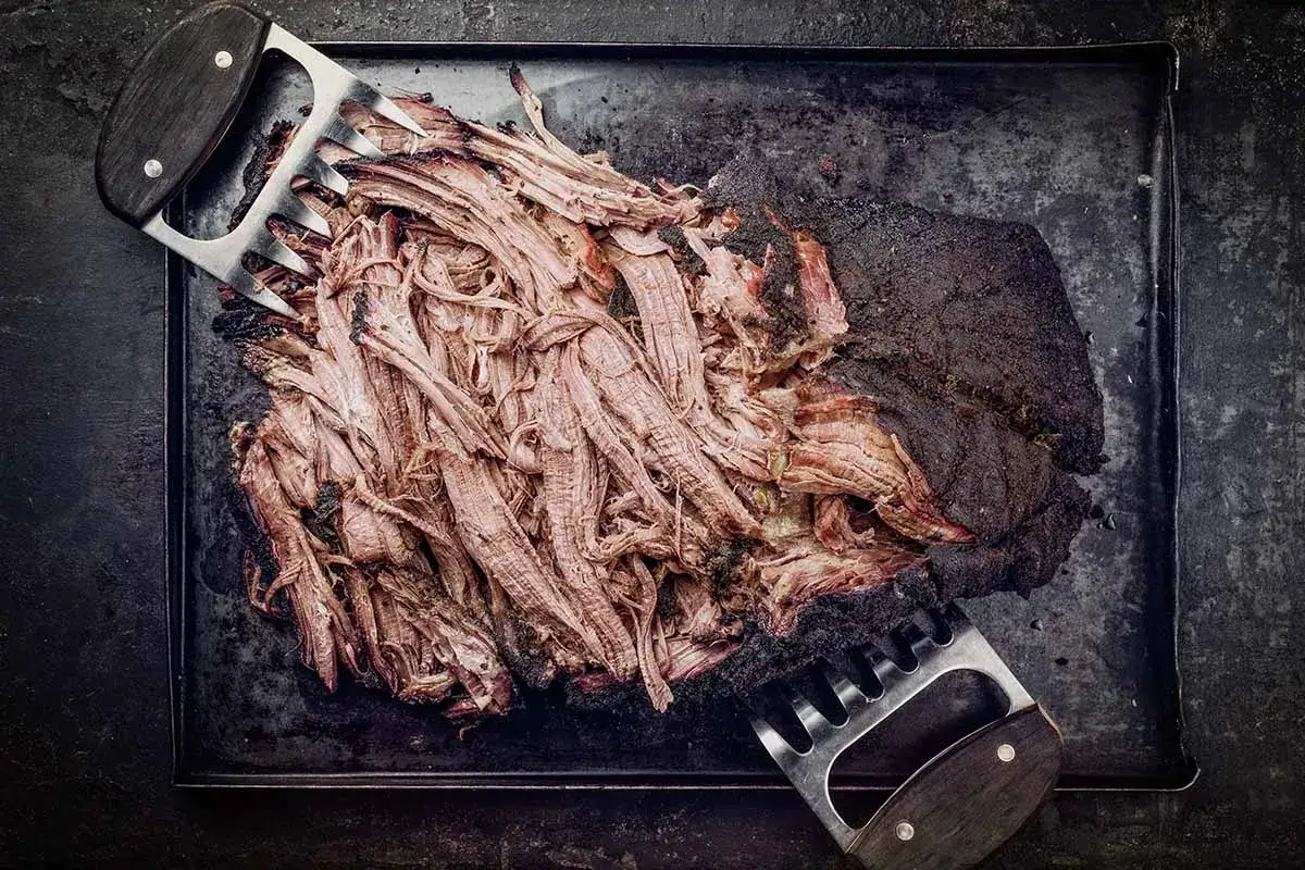 Zartes pulled beef, frisch aus dem Dutch Oven, wird mit Fleischkrallen zerteilt. Perfekt für BBQ!