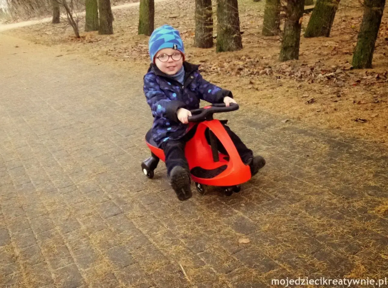 Uśmiechnięty chłopiec w czapce i okularach jeździ na czerwonym twistcarze. Od jakiego wieku można zacząć zabawę?