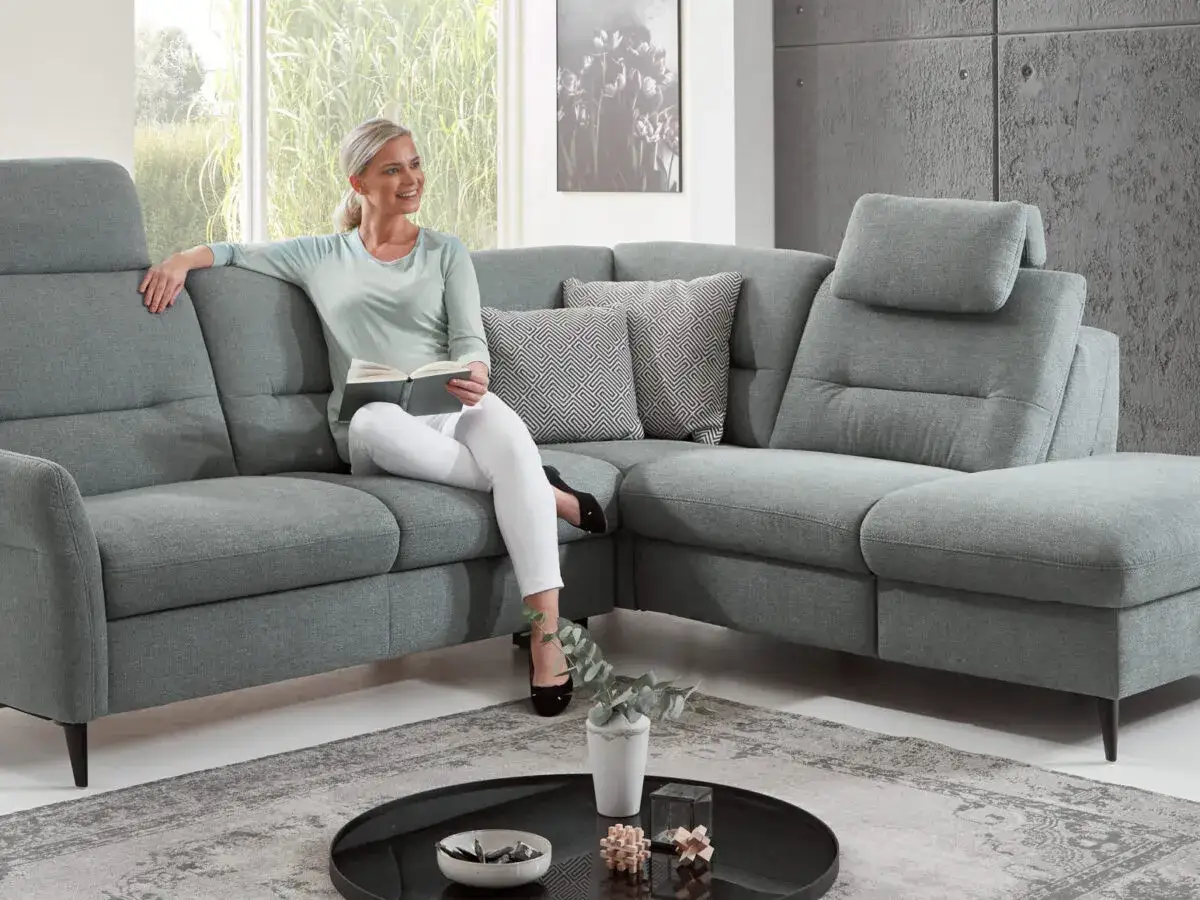 Frau liest auf einem bequemen Ecksofa mit tiefer sitztiefe. Das graue Sofa lädt zum Entspannen ein.