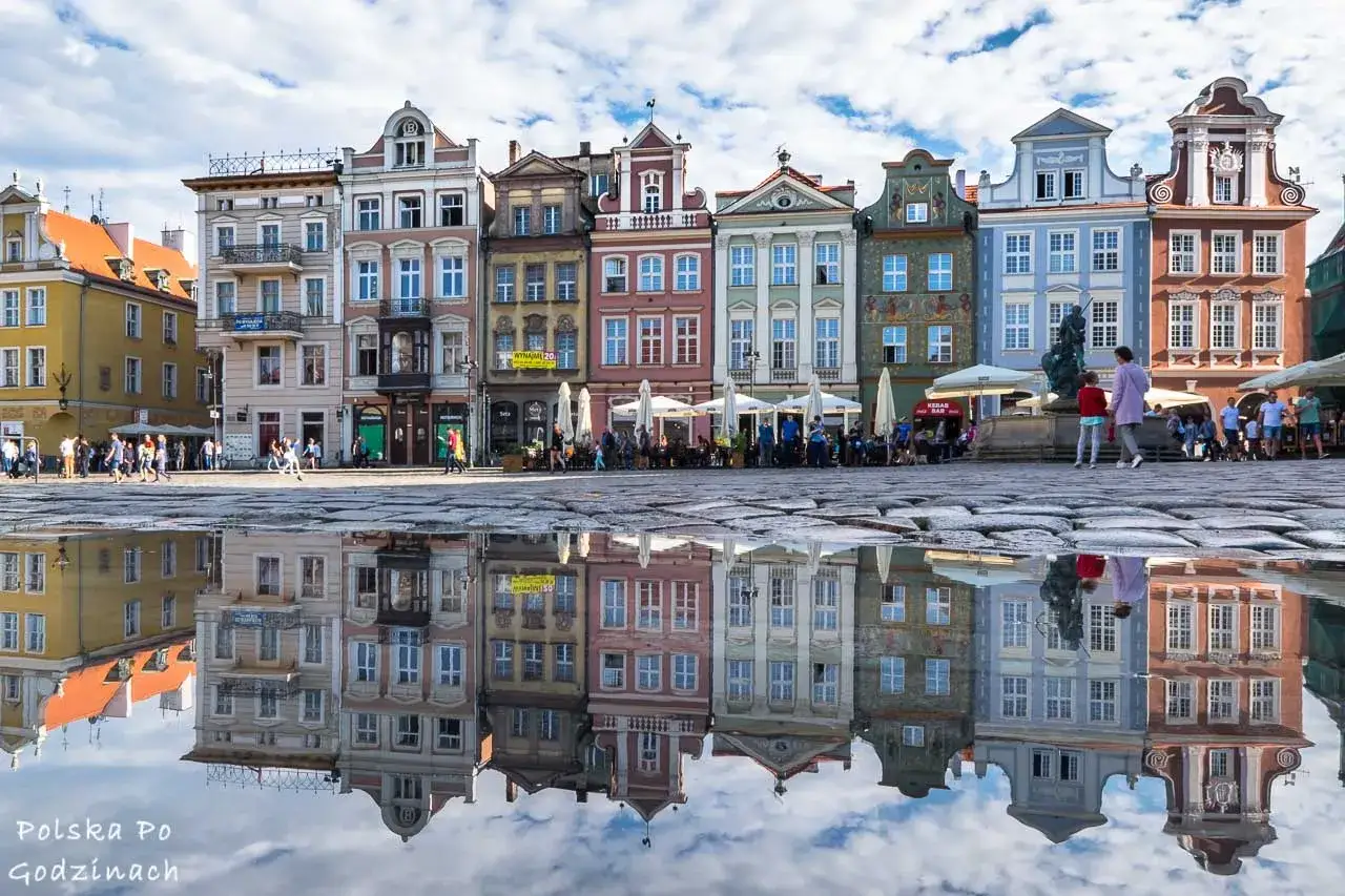 Kolorowe kamienice na Starym Rynku w Poznaniu, odbijające się w kałuży, idealne poznańskie atrakcje na weekend.
