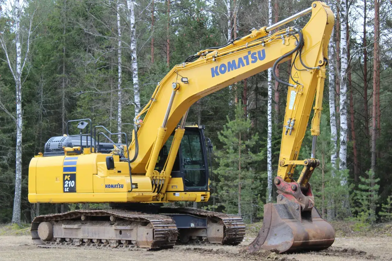 Żółta koparka gąsienicowa Komatsu PC 210 LC gotowa do pracy w lesie.