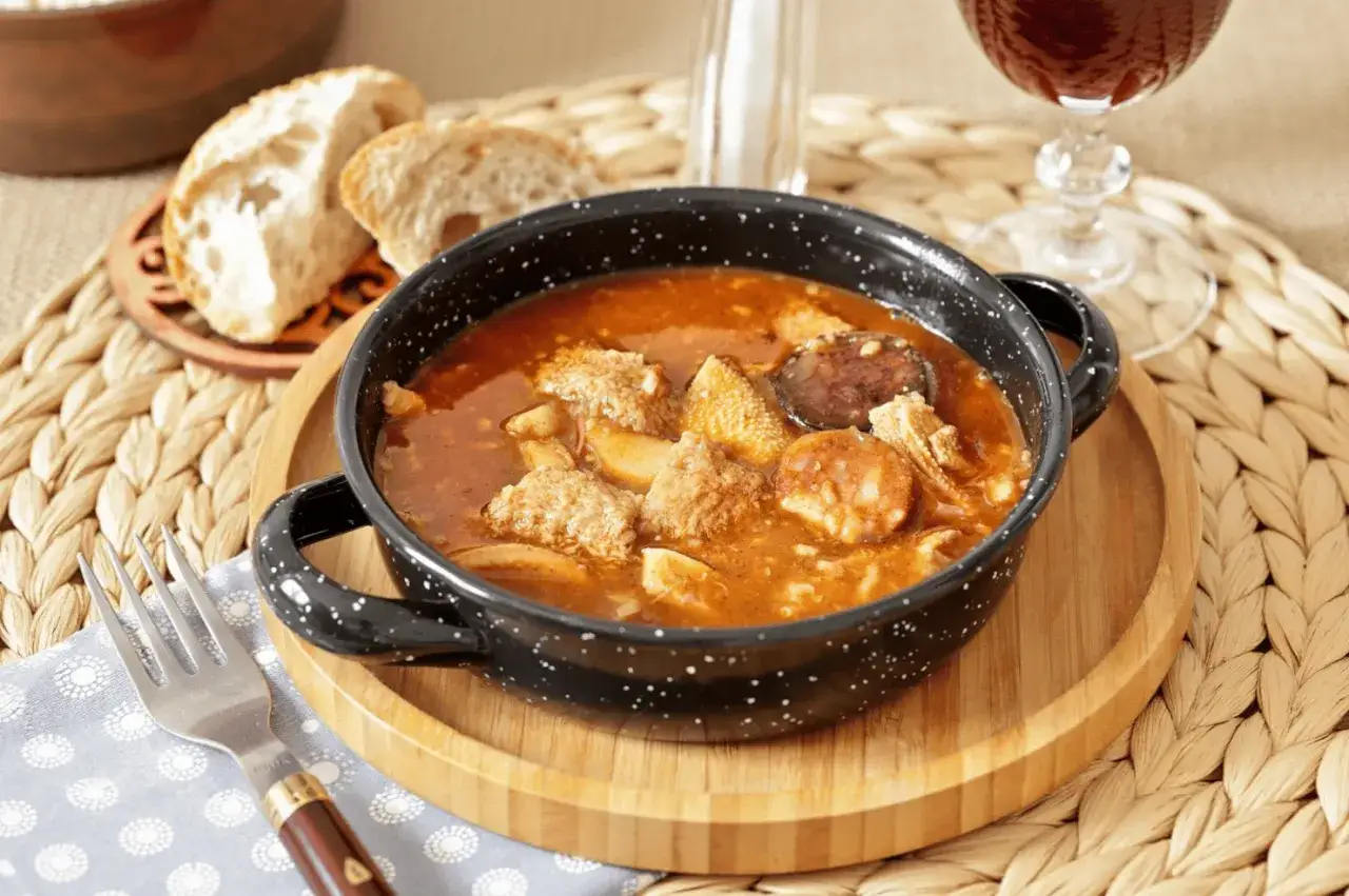 Un plato humeante de callos a la madrile&ntilde;a, con trozos de chorizo y pan r&uacute;stico al lado, listo para disfrutar.