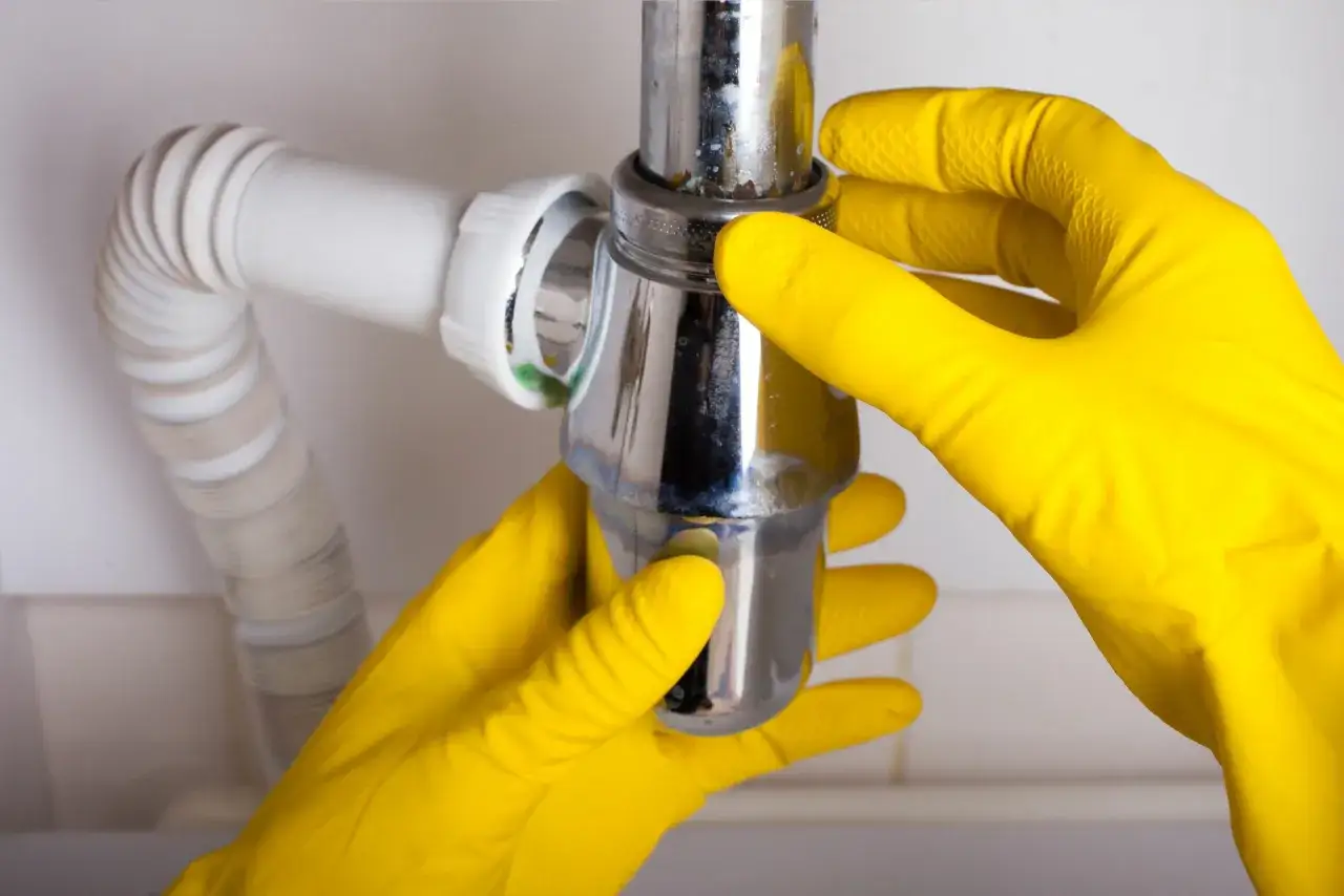 Mains jaunes pour r&eacute;parer un siphon qui fuit.