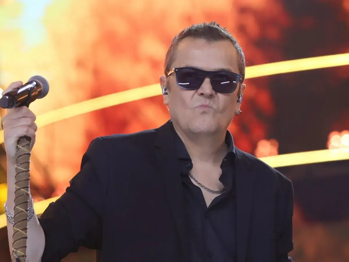 Artysta w okularach przeciwsłonecznych, z mikrofonem w dłoni, jakby śpiewał o wilkach dw&oacute;ch siostrach.