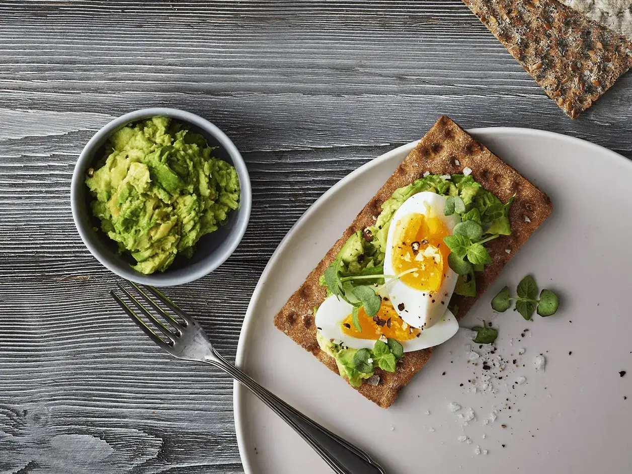 Un delicioso sandwich de aguacate y huevo, con un toque de pimienta y hierbas frescas, listo para disfrutar.
