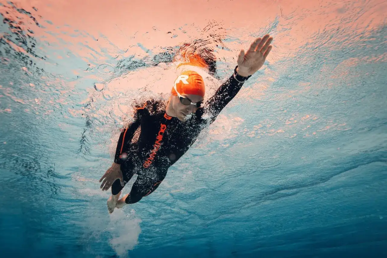 Underwater shot of a man in a wetsuit and orange cap performing triathlon swim workouts.