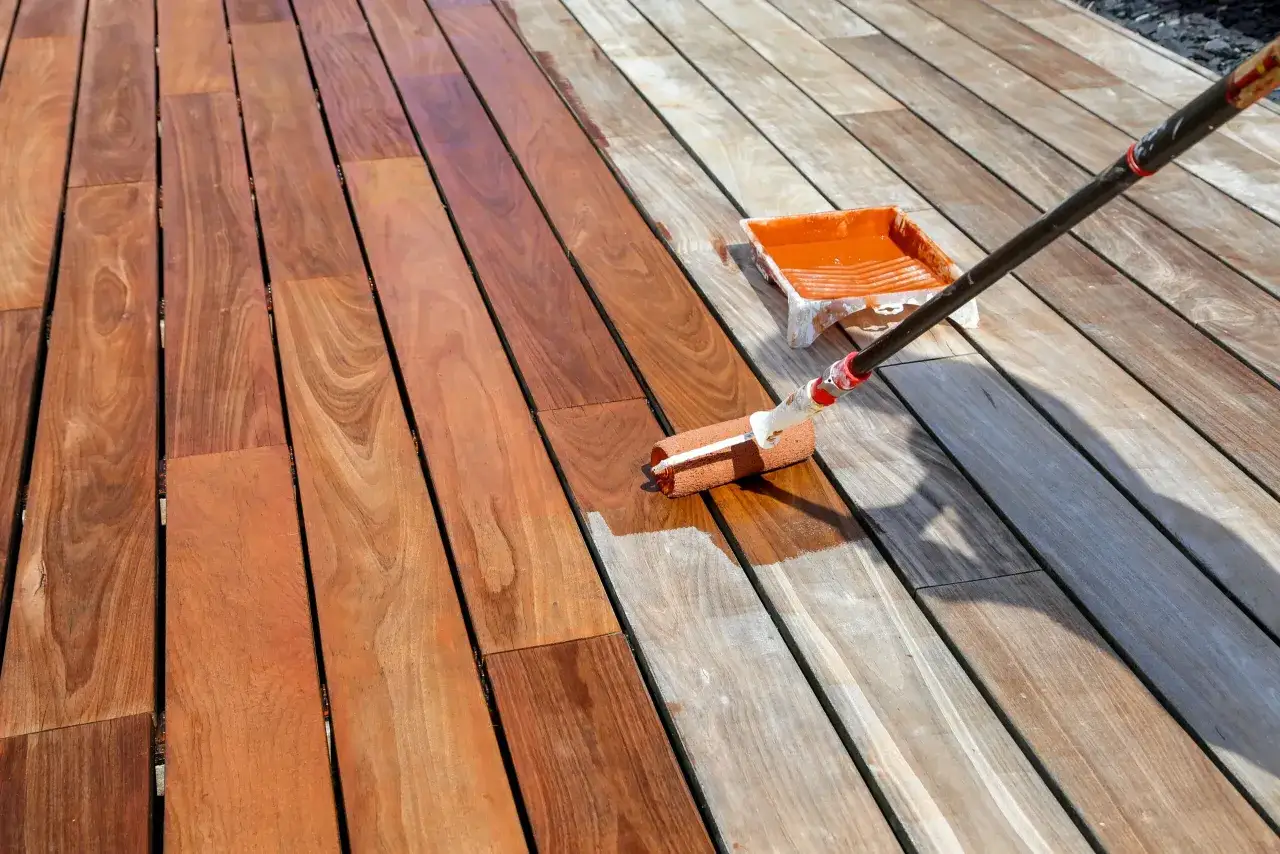 Application d'un saturateur bois int&eacute;rieur sur une terrasse en bois. Le rouleau d&eacute;pose le produit, transformant le bois gris&acirc;tre en une teinte chaude et protectrice.