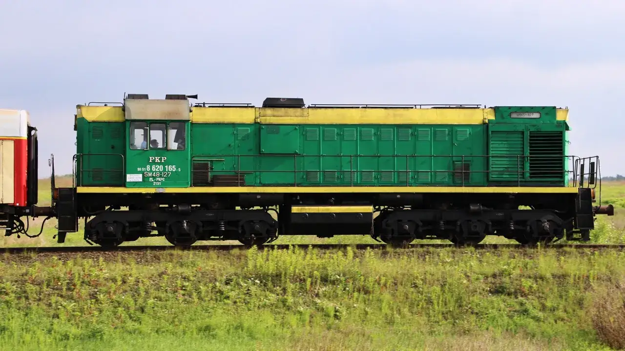 Zielona lokomotywa SM48-127 PKP z żółtym pasem jedzie po torach wśród zielonej trawy.