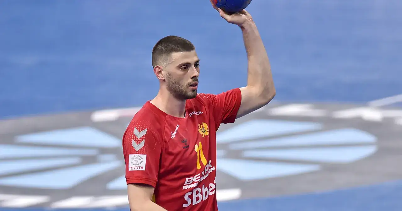 Branko Vujović, zawodnik piłki ręcznej, w czerwonej koszulce z numerem 11, trzyma piłkę nad głową.