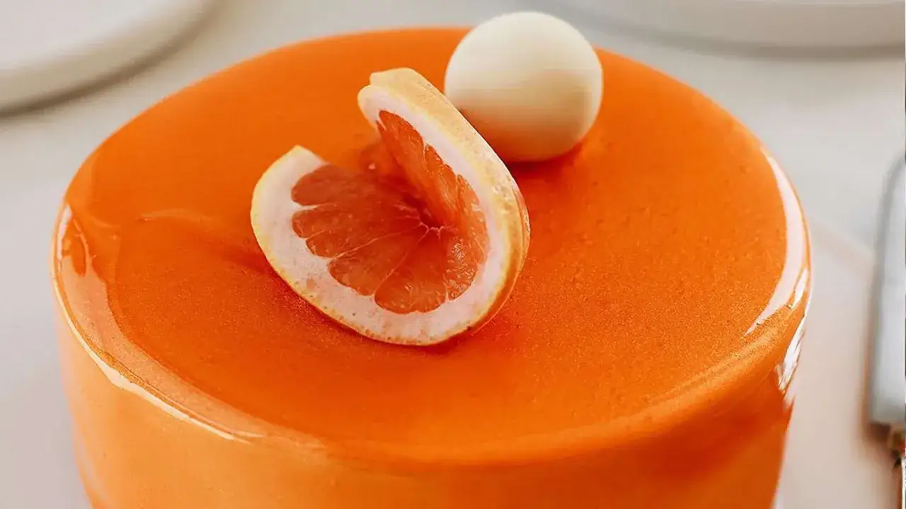 G&acirc;teau rond au gla&ccedil;age miroir orange vif, d&eacute;cor&eacute; d'une tranche de pamplemousse et d'une sph&egrave;re blanche.