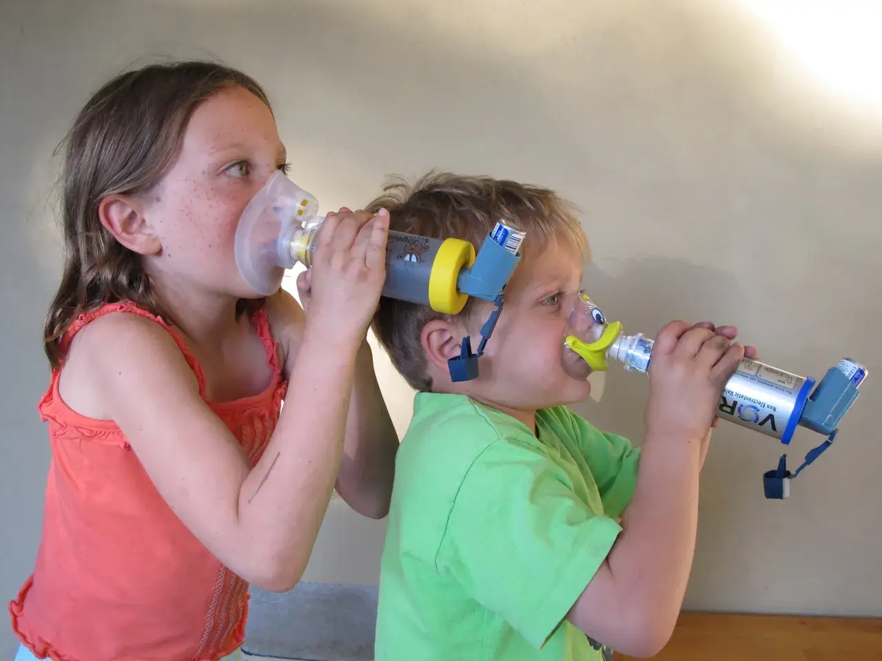 Bambini con inalatori per gestire il broncospasmo. La bambina usa una maschera, il bambino un adattatore a forma di papera.