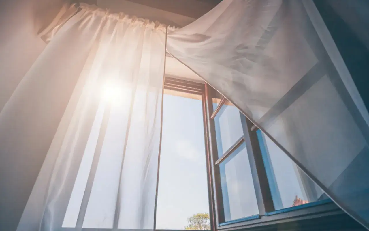 Tende leggere svolazzano con la brezza estiva attraverso finestre aperte o chiuse, lasciando filtrare la luce del sole.