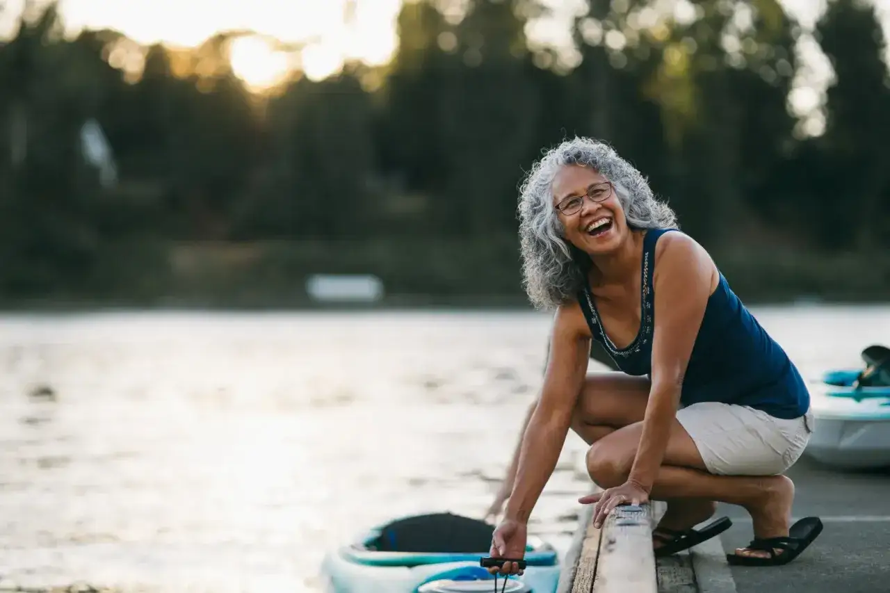 Une femme rit en s'accroupissant près d'un kayak, incarnant la mobilité douce définition.
