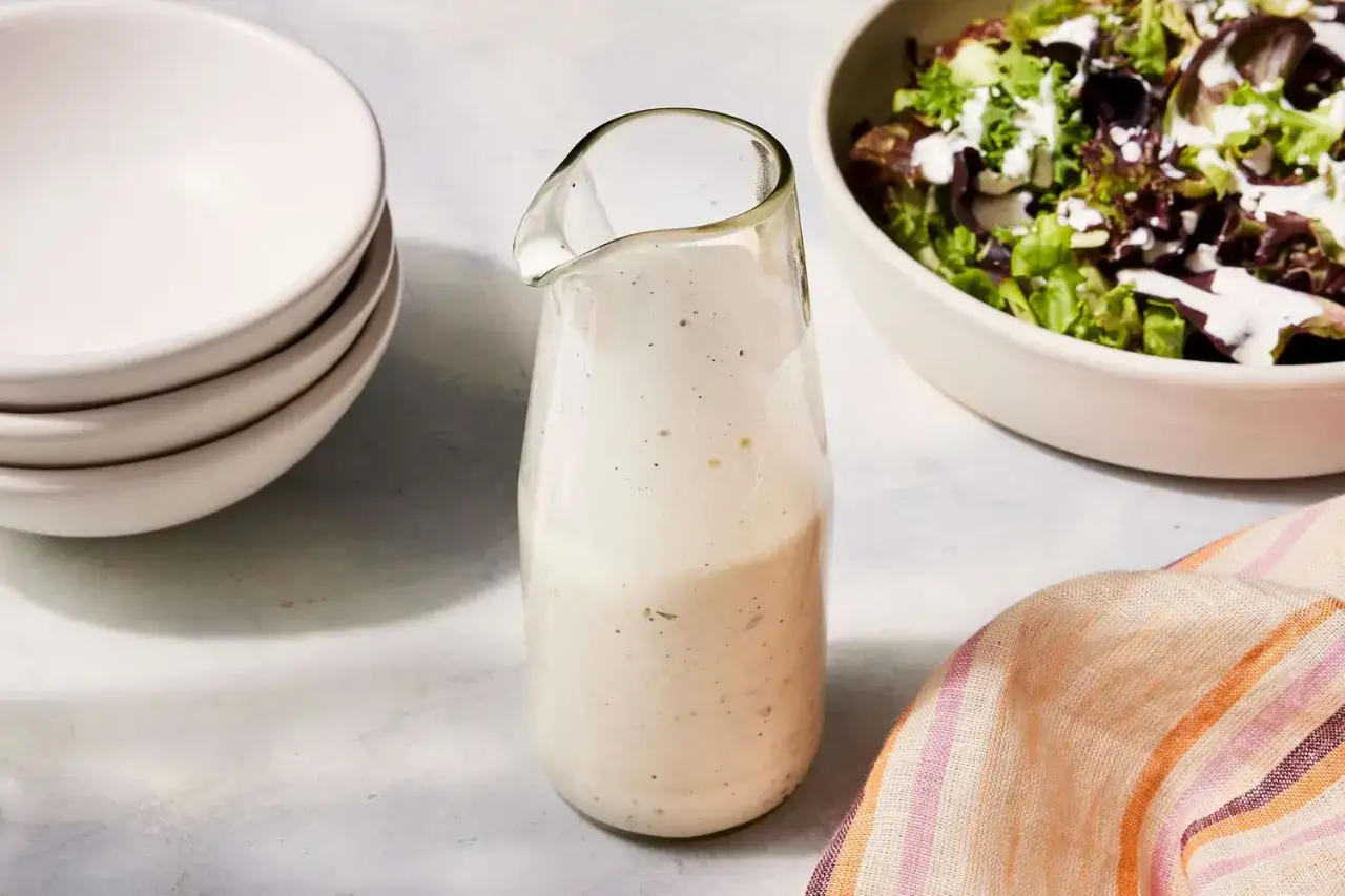 Ein Glas mit cremiger Ranch-Dressing steht neben einer Schüssel Salat.
