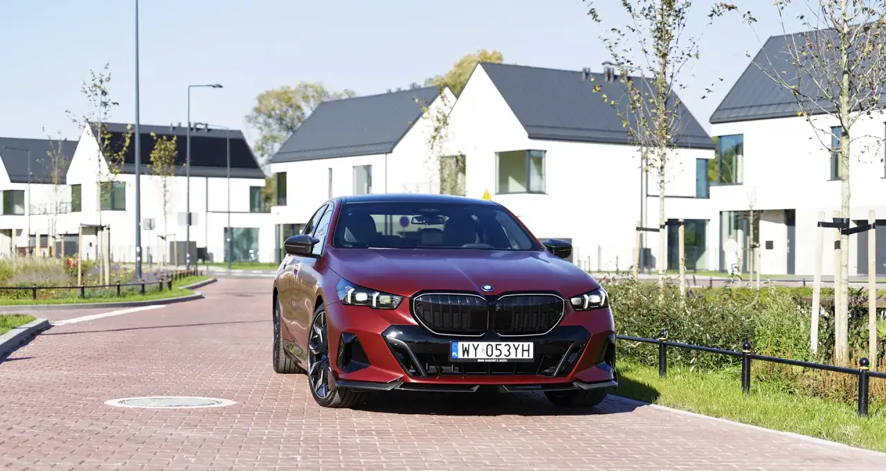 Czerwone BMW 550e na tle nowoczesnych domów z panelami słonecznymi.