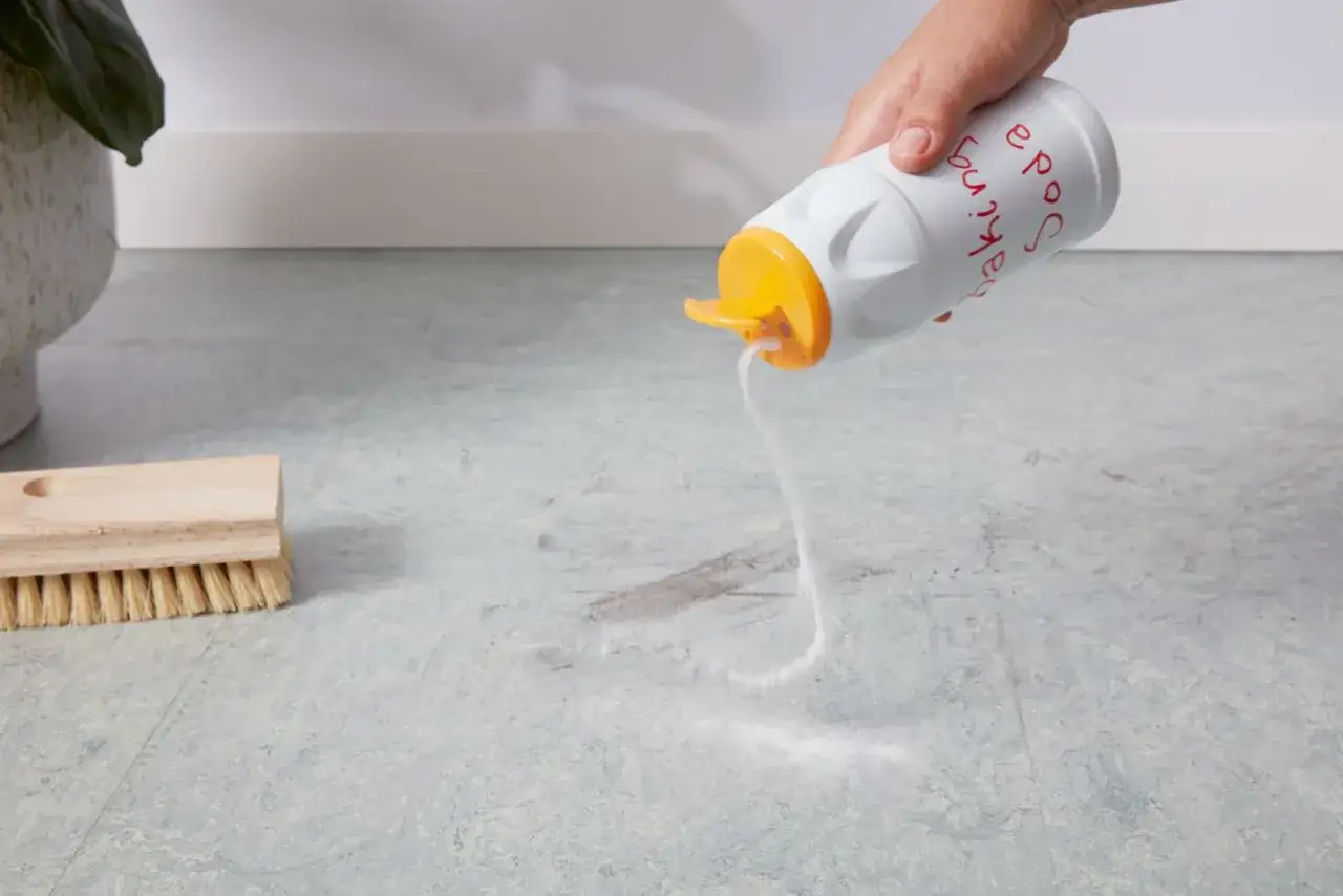 Saupoudrer du bicarbonate de soude pour enlever peinture sur lino. Une brosse est à côté.