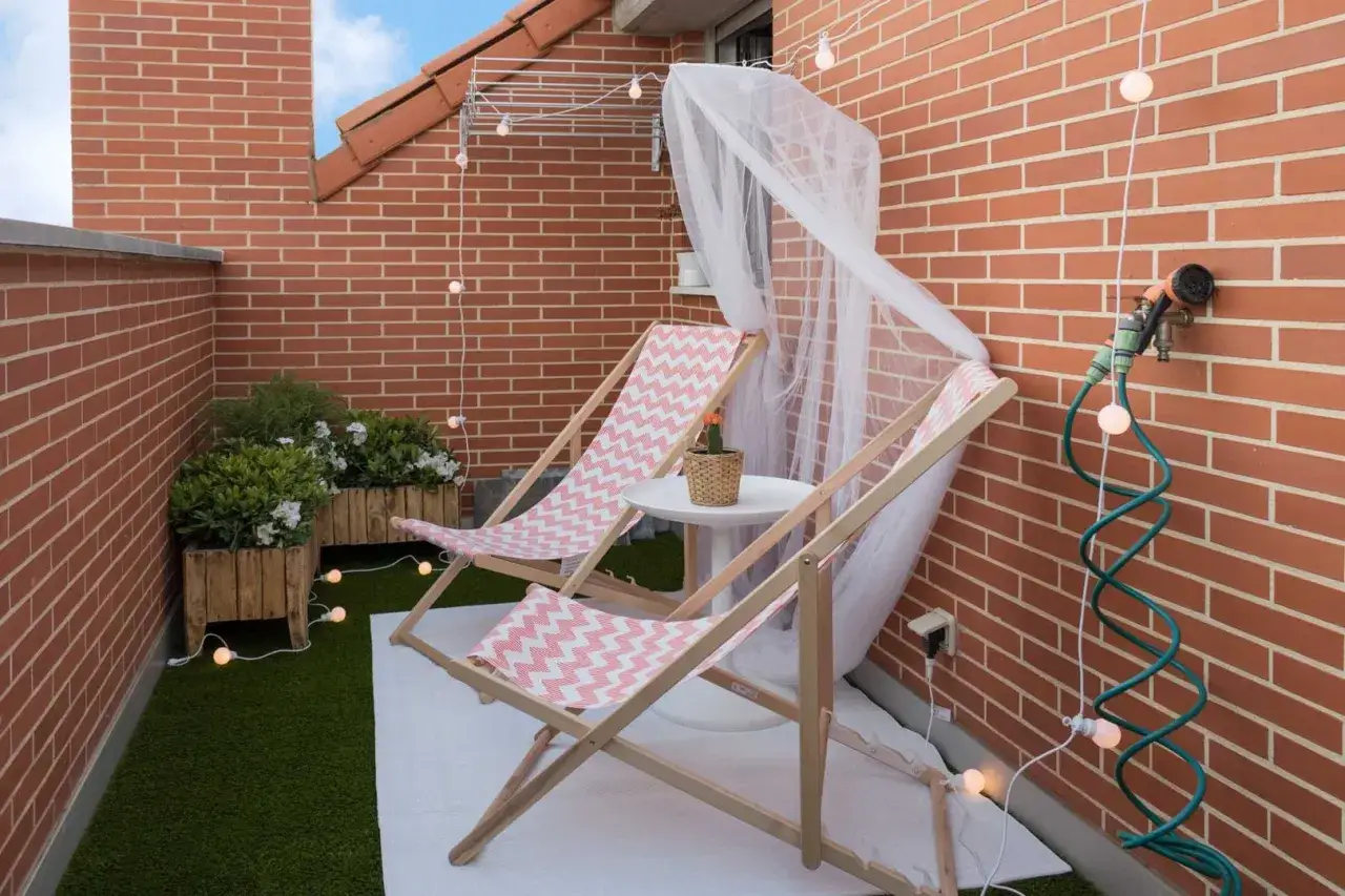 Acogedora terraza de 10 metros cuadrados con dos tumbonas, plantas y luces decorativas. Ideal para relajarse al aire libre.
