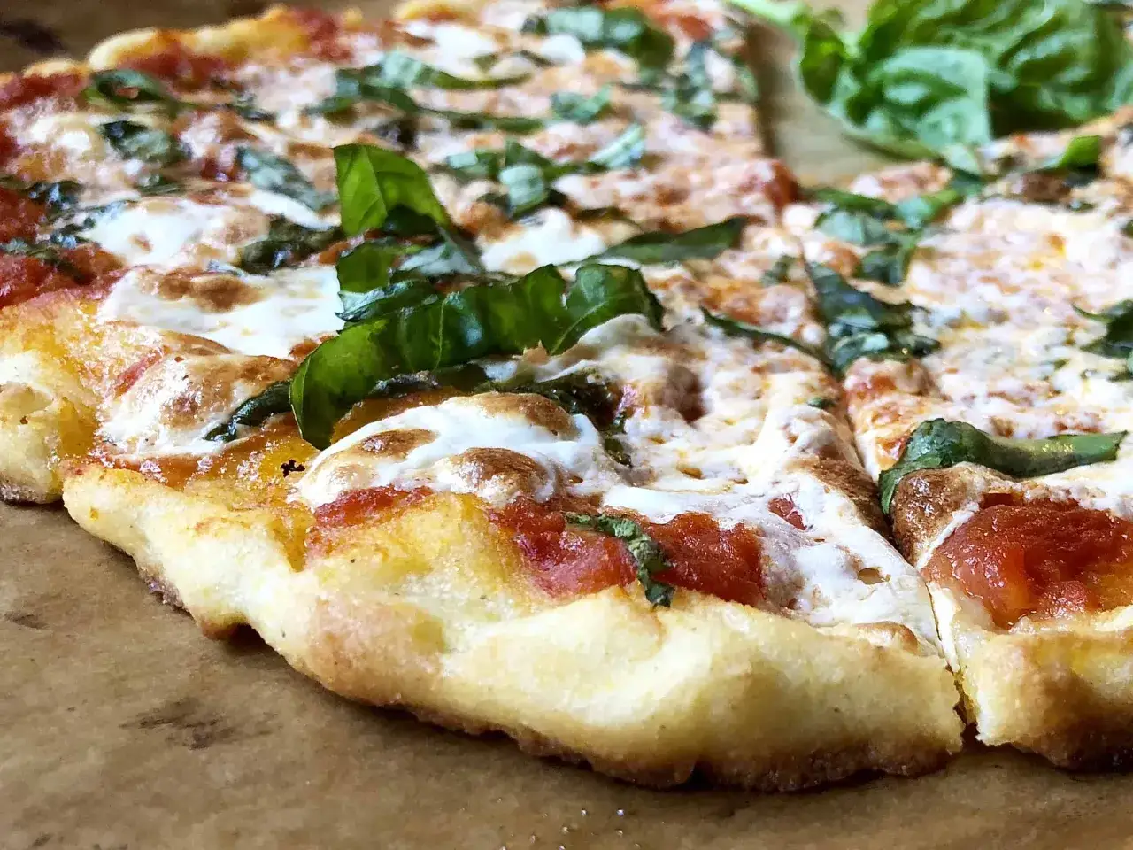 En n&auml;rbild av en glutenfri pizza med sm&auml;lt ost, tomats&aring;s och f&auml;rsk basilika. Ett perfekt glutenfri pizzadeg recept!
