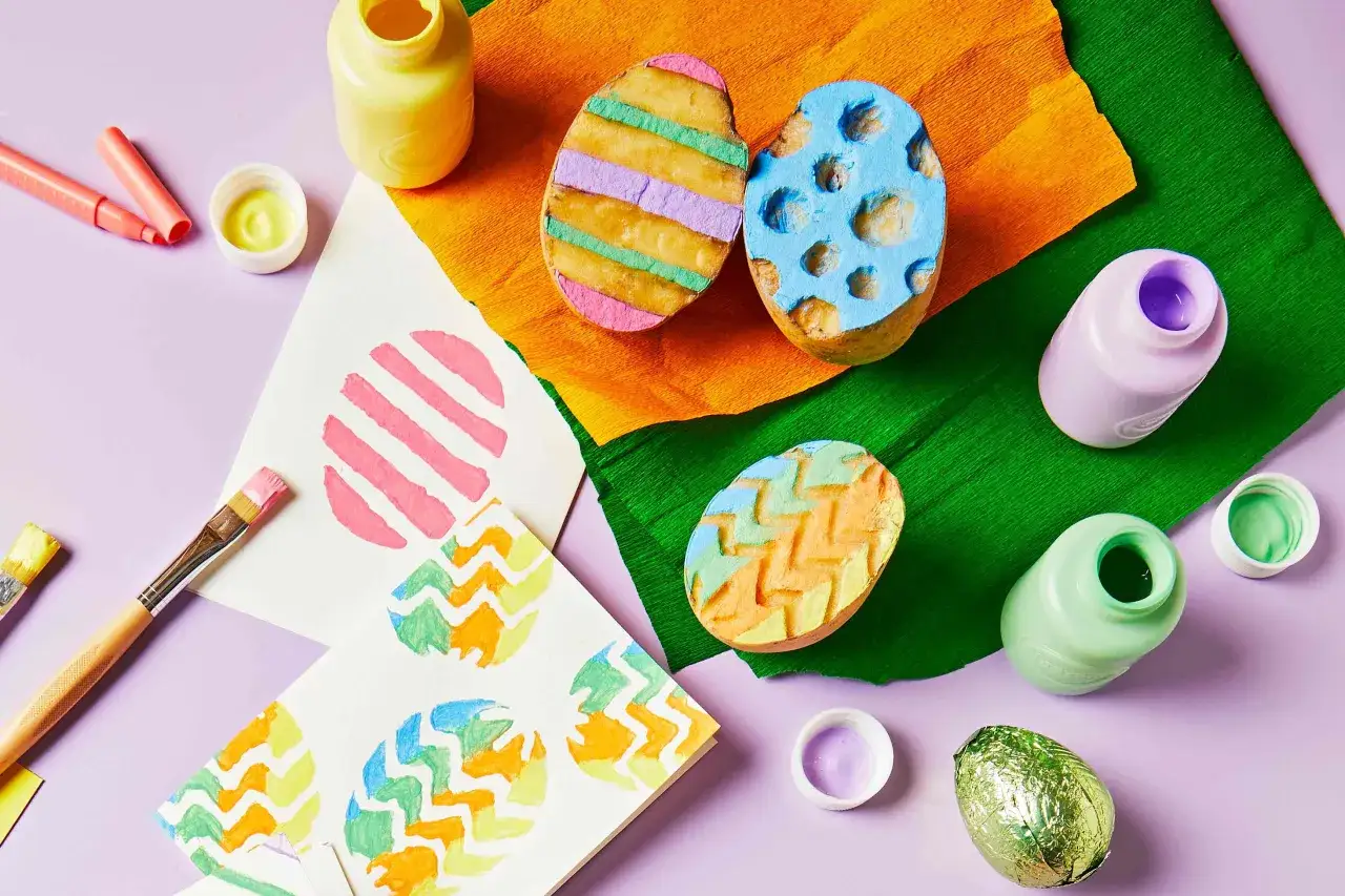 Bunte Kartoffelstempel mit Fingerfarbe Ostern-Motiven, Pinsel und Farben liegen bereit für kreative Osterdekorationen.