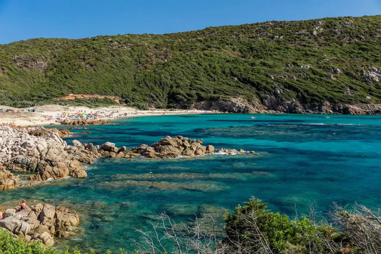 Vue idyllique de **mare e monti** : une plage animée bordée par une mer turquoise et une colline verdoyante.