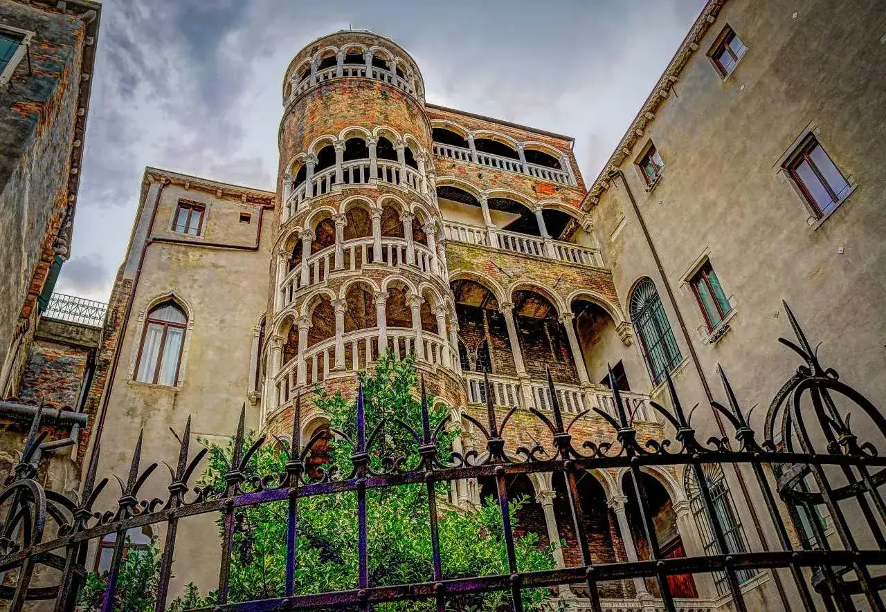La Torre del Bovolo, un gioiello architettonico veneziano, si erge maestosa con la sua scala a chiocciola esterna, circondata da edifici storici e un cancello in ferro battuto.