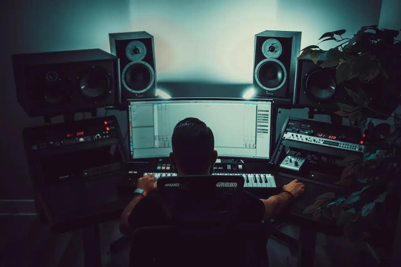 Mann am Computer, umgeben von Lautsprechern und Equipment, vertieft in den **sound mixing** Prozess.