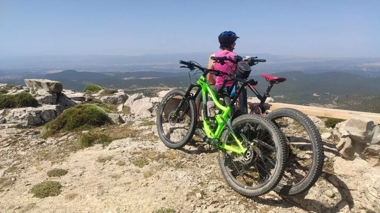 Dos bicicletas de monta&ntilde;a descansan en la cima, contemplando las **monta&ntilde;as vac&iacute;as** y el paisaje lejano.
