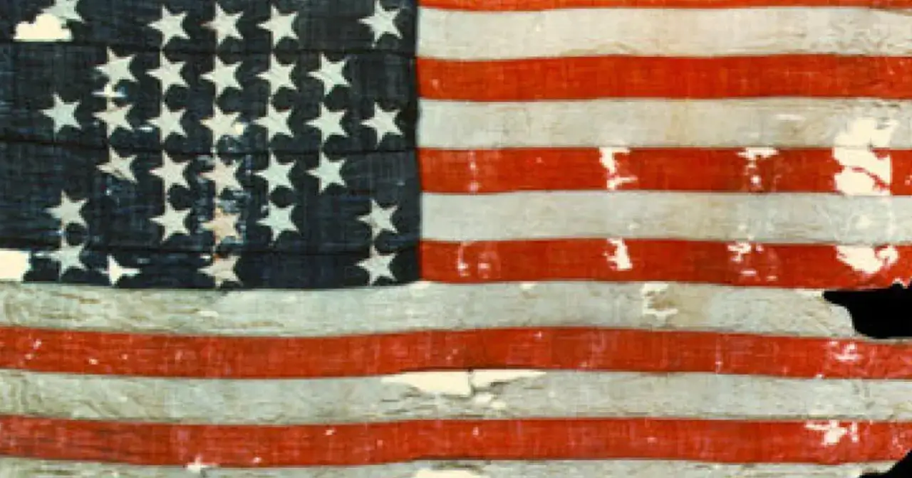 Fragment starej, zniszczonej flagi USA, z widocznymi gwiazdami i pasami. To może być pierwsza flaga USA, świadectwo historii.
