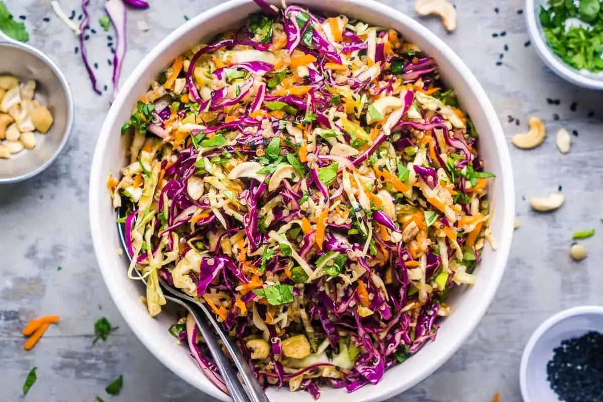 En f&auml;rgglad asiatisk k&aring;lsallad med r&ouml;dk&aring;l, mor&ouml;tter, n&ouml;tter och &ouml;rter i en vit sk&aring;l.
