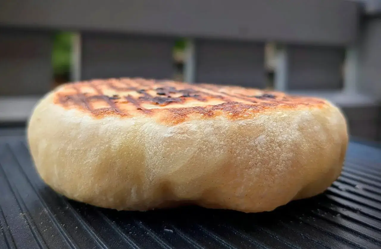 Ein goldbraunes Grillbrot mit typischen Grillstreifen liegt auf einem Grillrost. Perfekt f&uuml;r dein Grillbrot Rezept!