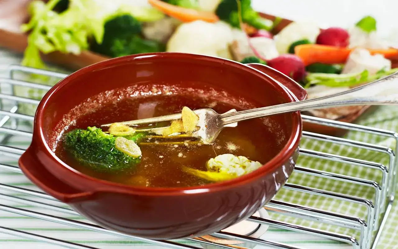 En skål med varm buljong och grönsaker, som broccoli och blomkål, med en gaffel i. En härlig bagna cauda-inspirerad rätt.