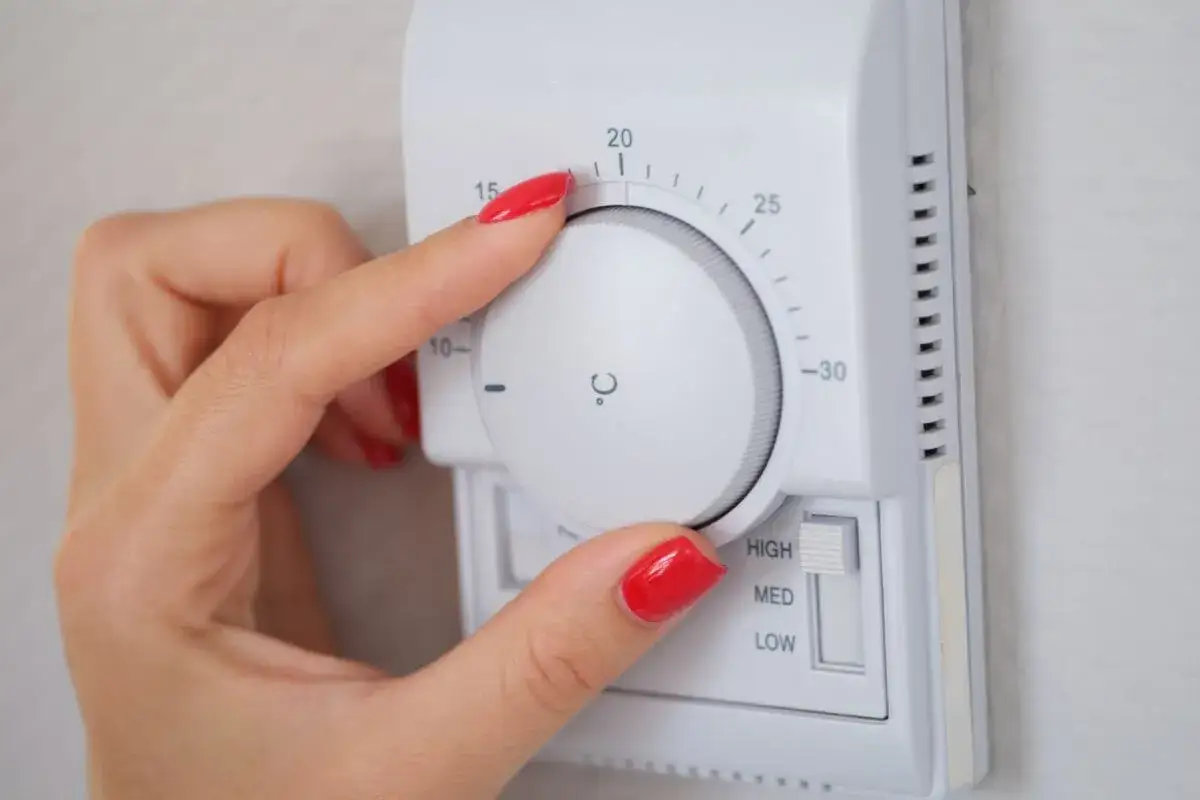 Mano con uñas rojas ajustando el termostato. Es hora de encender la calefacción y poner la temperatura a 20 grados.