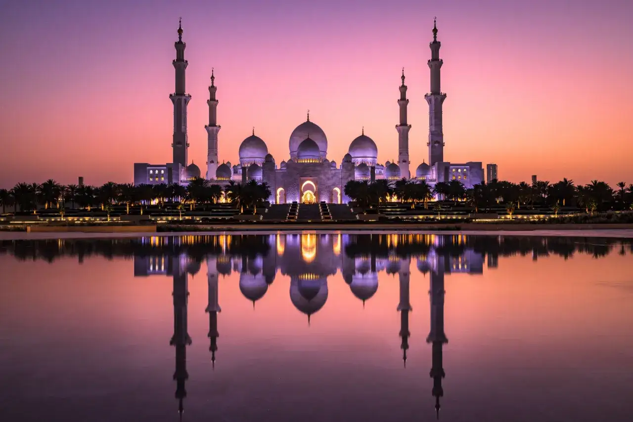 Scheich-Zayid-Moschee in Abu Dhabi bei Sonnenuntergang, ein Muss für Abu Dhabi Tipps. Die Moschee spiegelt sich im Wasser.