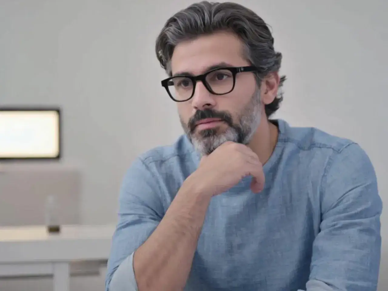Uomo con barba e capelli grigi, indossa occhiali neri. Sembra pensare, con un leggero vedere sfocato con occhiali nuovi.