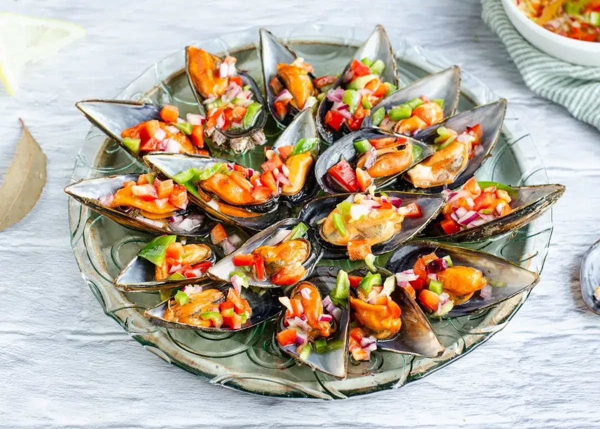 Mejillones a la vinagreta, frescos y coloridos, servidos en su concha con una picada de pimientos y cebolla.