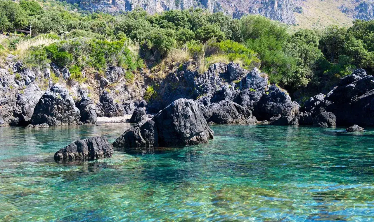 Acque cristalline e rocce scure incorniciano una piccola spiaggia a Maratea, immersa nel verde della macchia mediterranea.