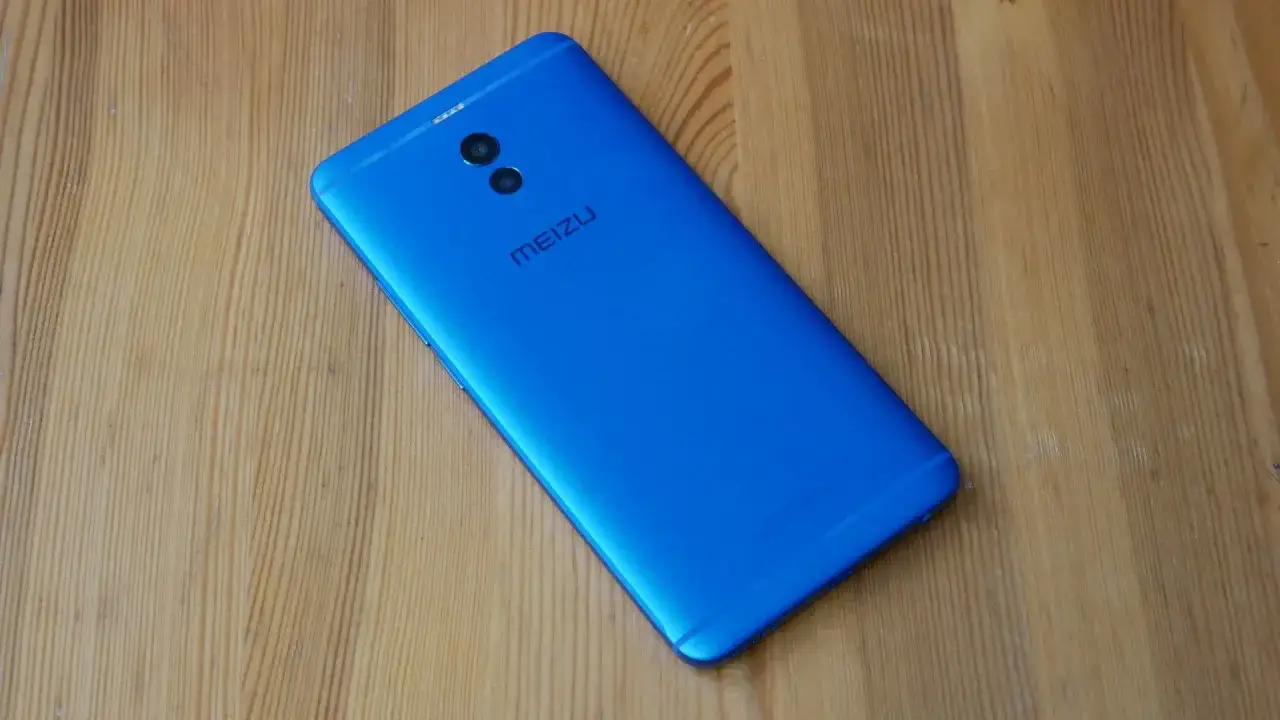 Niebieski smartfon Meizu M6 Note z podwójnym aparatem z tyłu leży na drewnianym blacie.